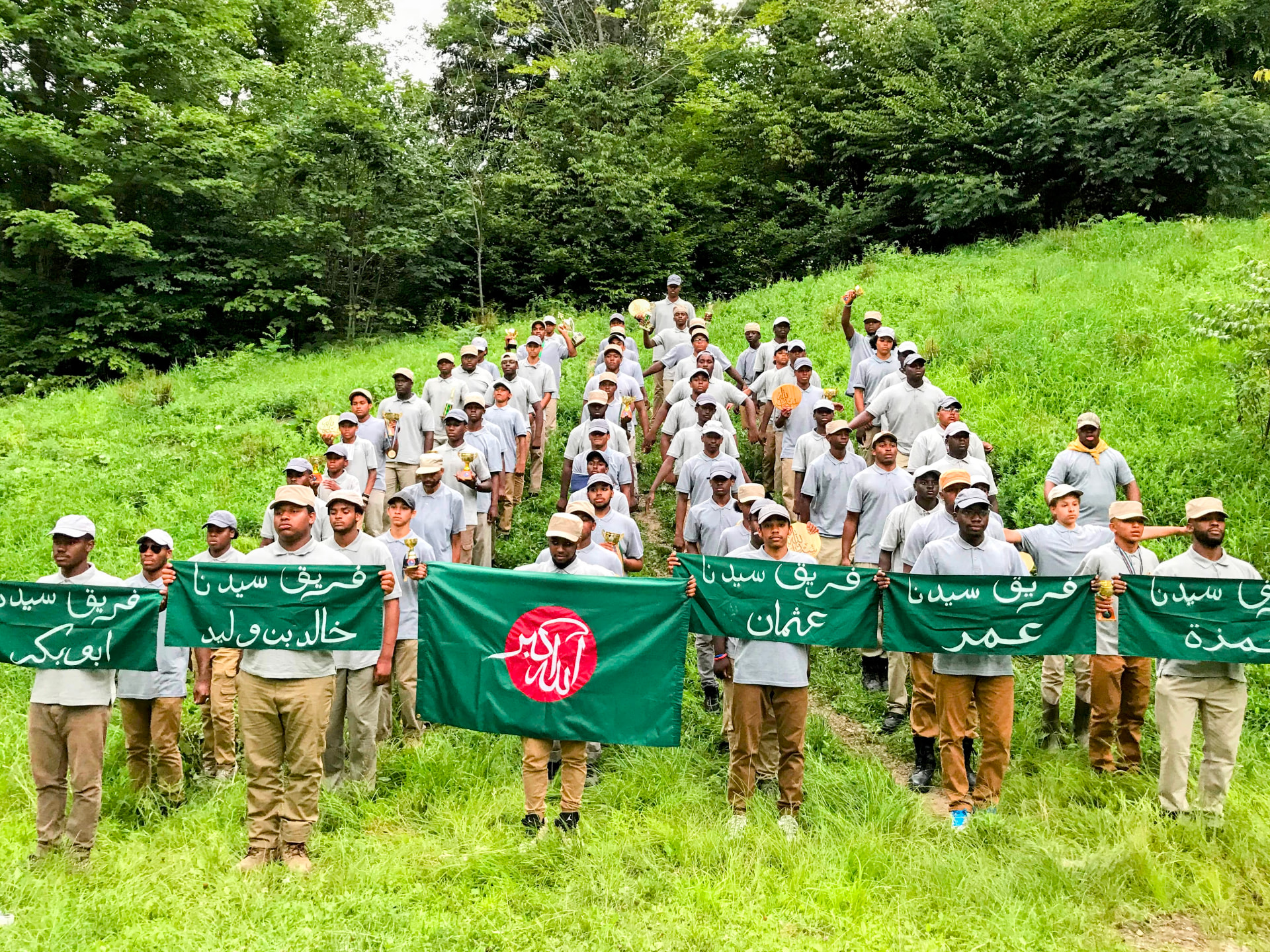Muslim Scouts of America members standing together on a green hillside holding team banners